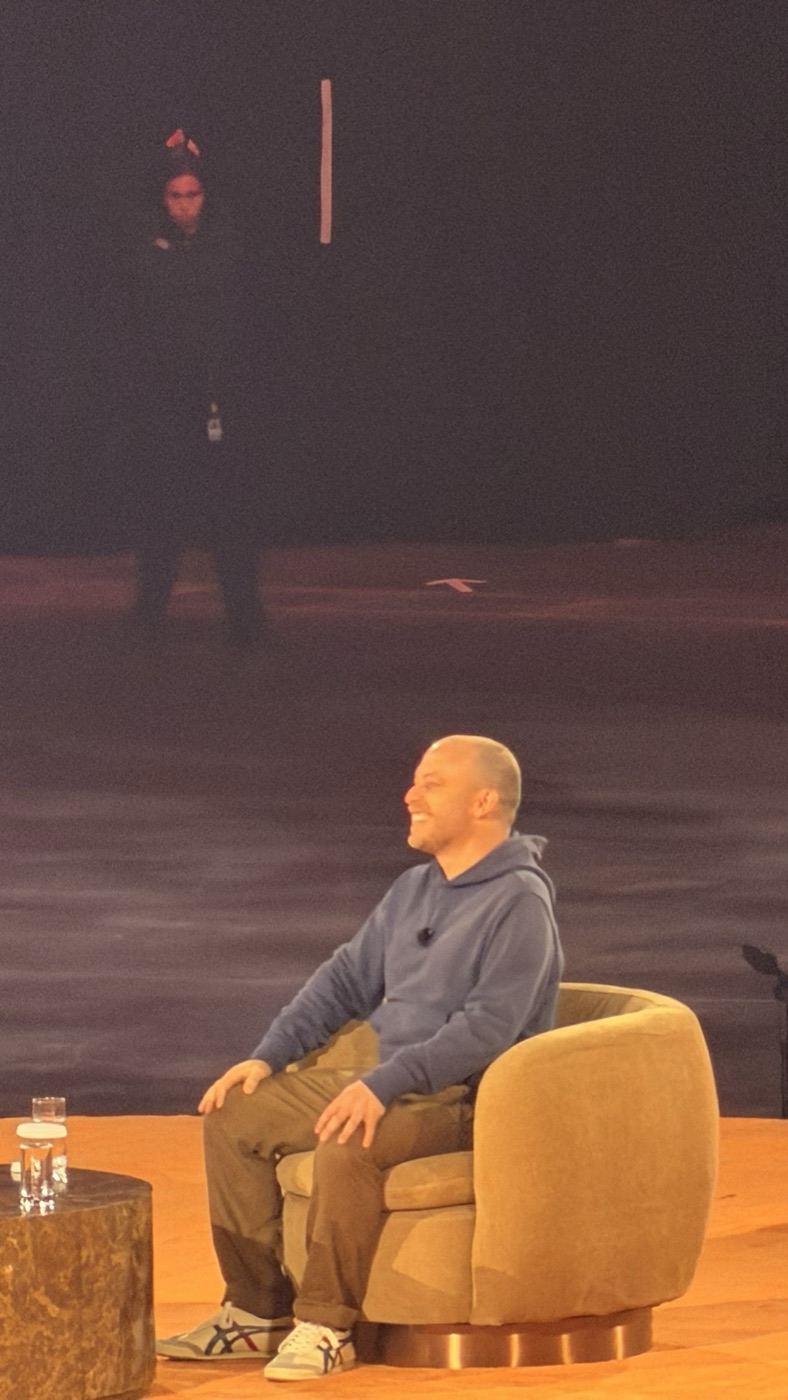 A speaker in a blue hoodie laughing in the armchair